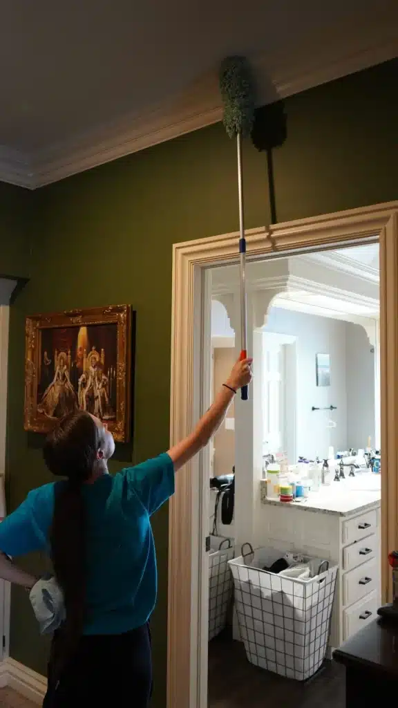 Woman cleaning high corners with a duster in a well-lit home, showcasing Simply Maid's professional cleaning services in Ramona, OK.