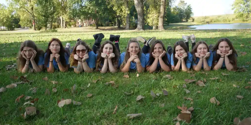 Group of smiling cleaning technicians in blue shirts lying on grass, promoting specialized cleaning services for film production in Tulsa.