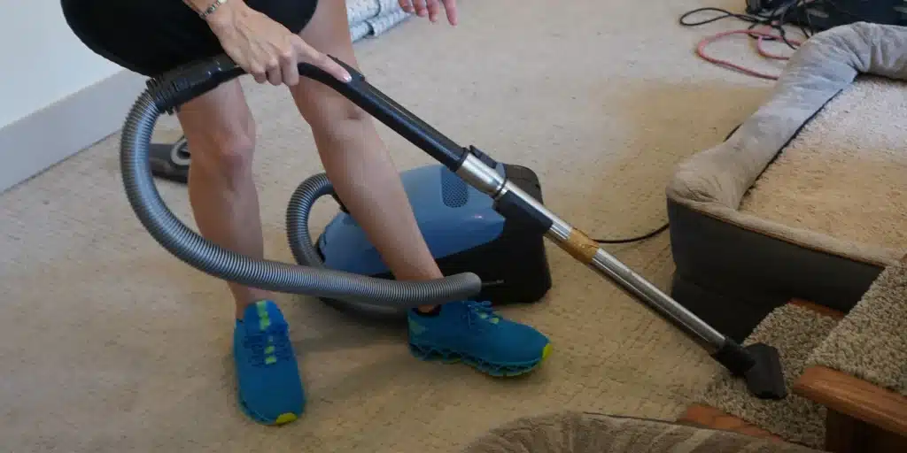 Person vacuuming carpet near furniture, demonstrating effective cleaning techniques for a tidy home environment.