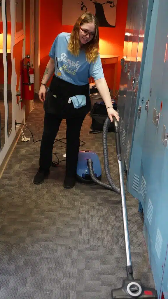 Simply Maid Sparkle Technician vacuuming a carpeted hallway